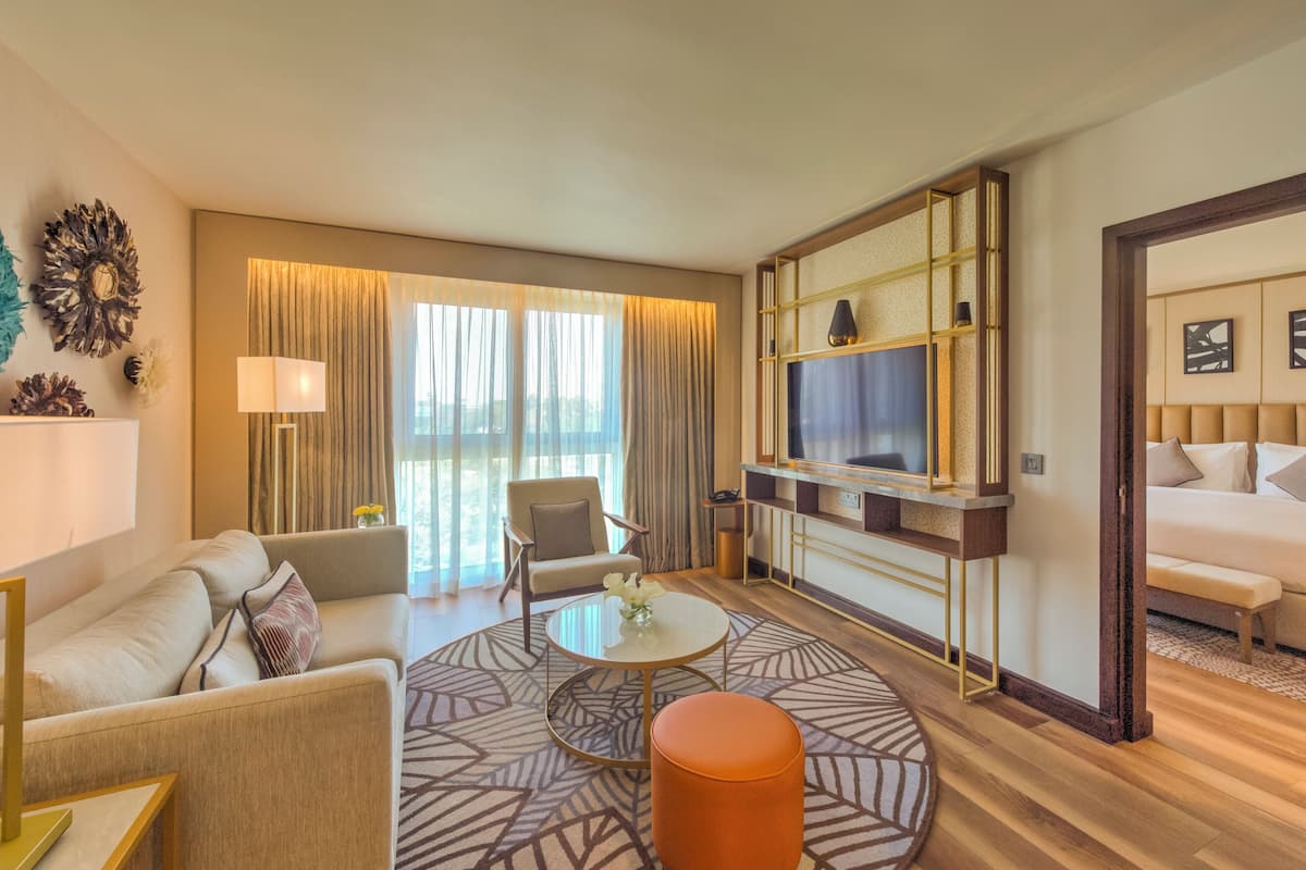 A modern hotel room with a sofa, armchair, round coffee table, and a TV mounted on a wall.
