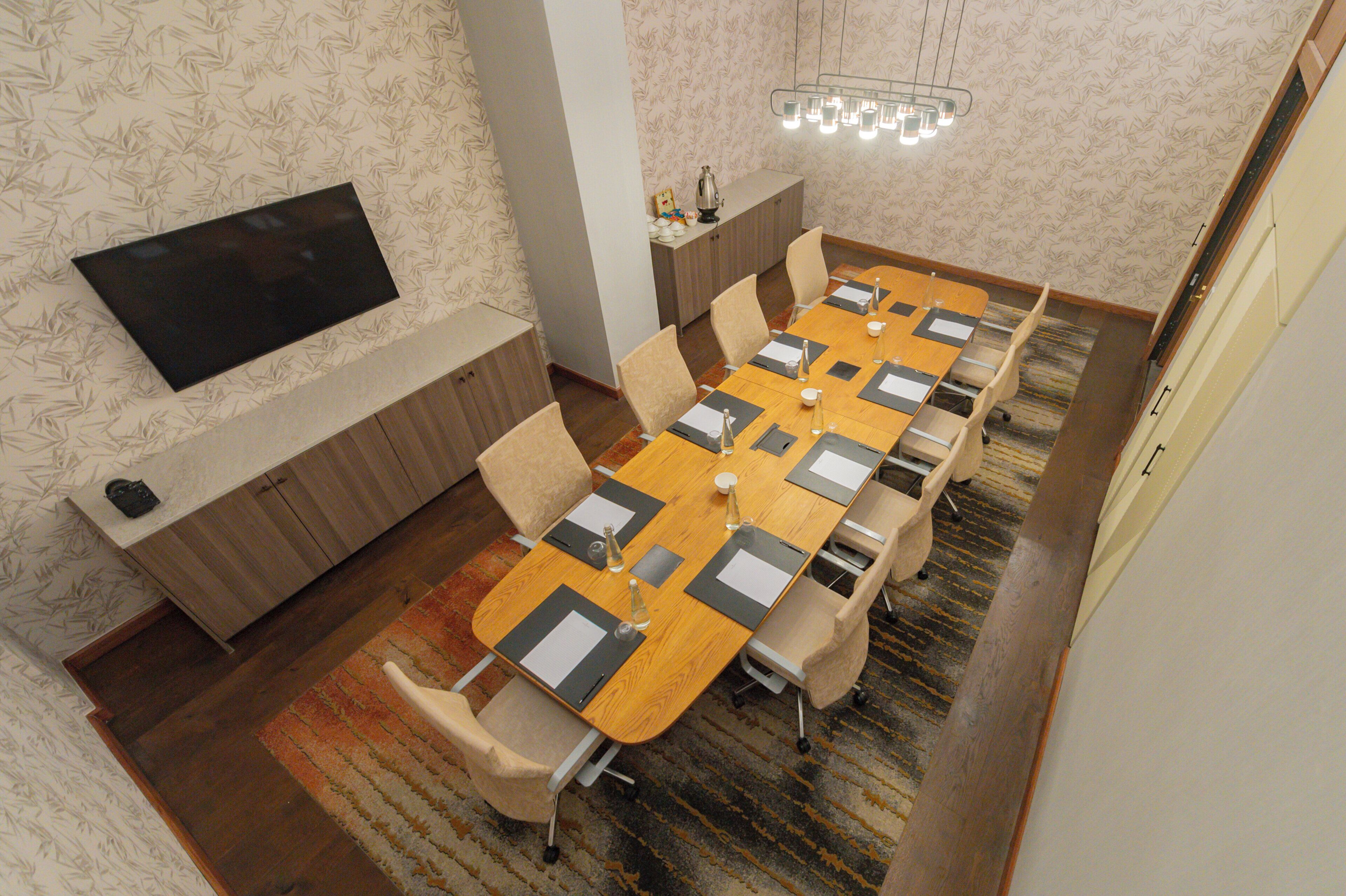 Une salle de conférence avec une longue table, des chaises, un téléviseur et un mur décoré de motifs.