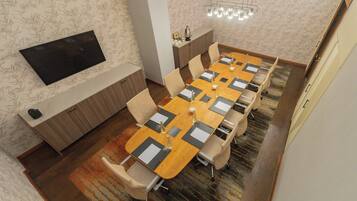 Une salle de conférence avec une longue table, des chaises, un téléviseur et un mur décoré de motifs.