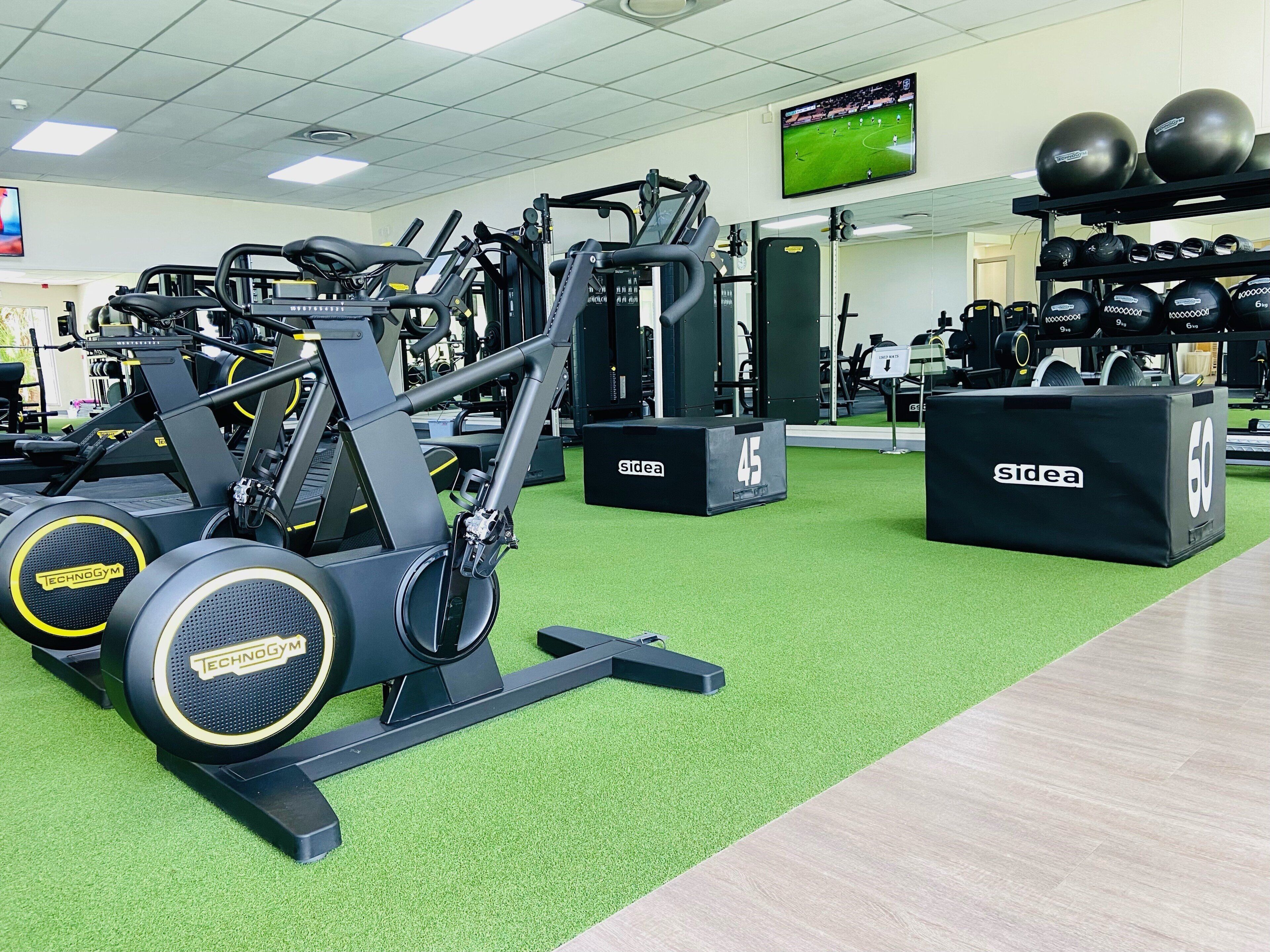 A gym with exercise equipment, a television screen, and weightlifting balls.