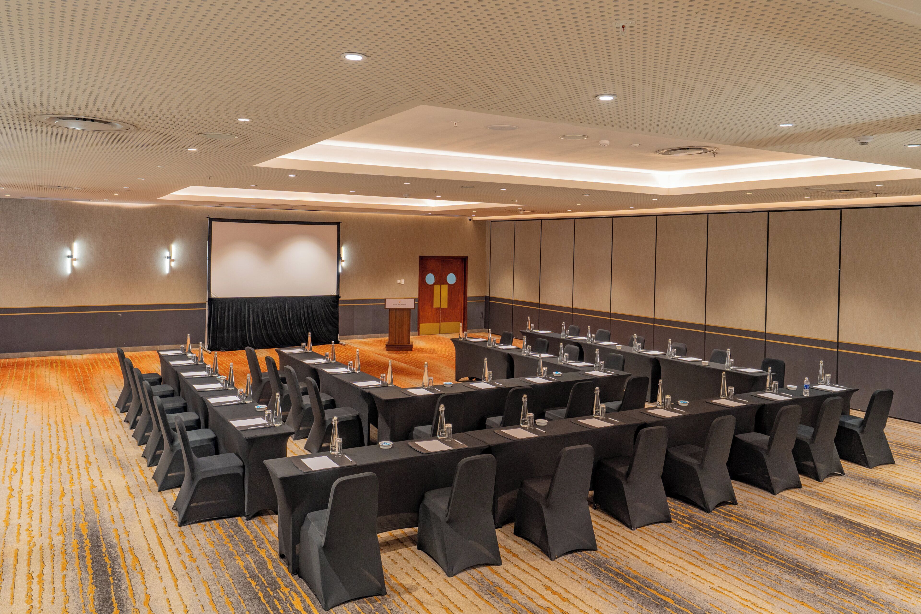 A conference room with a long table, chairs, a podium, and a screen.
