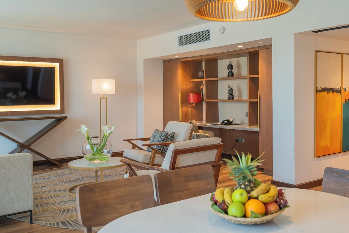 Una sala de estar moderna con comedor, que incluye un televisor de pantalla plana grande, asientos cómodos y un frutero sobre la mesa.