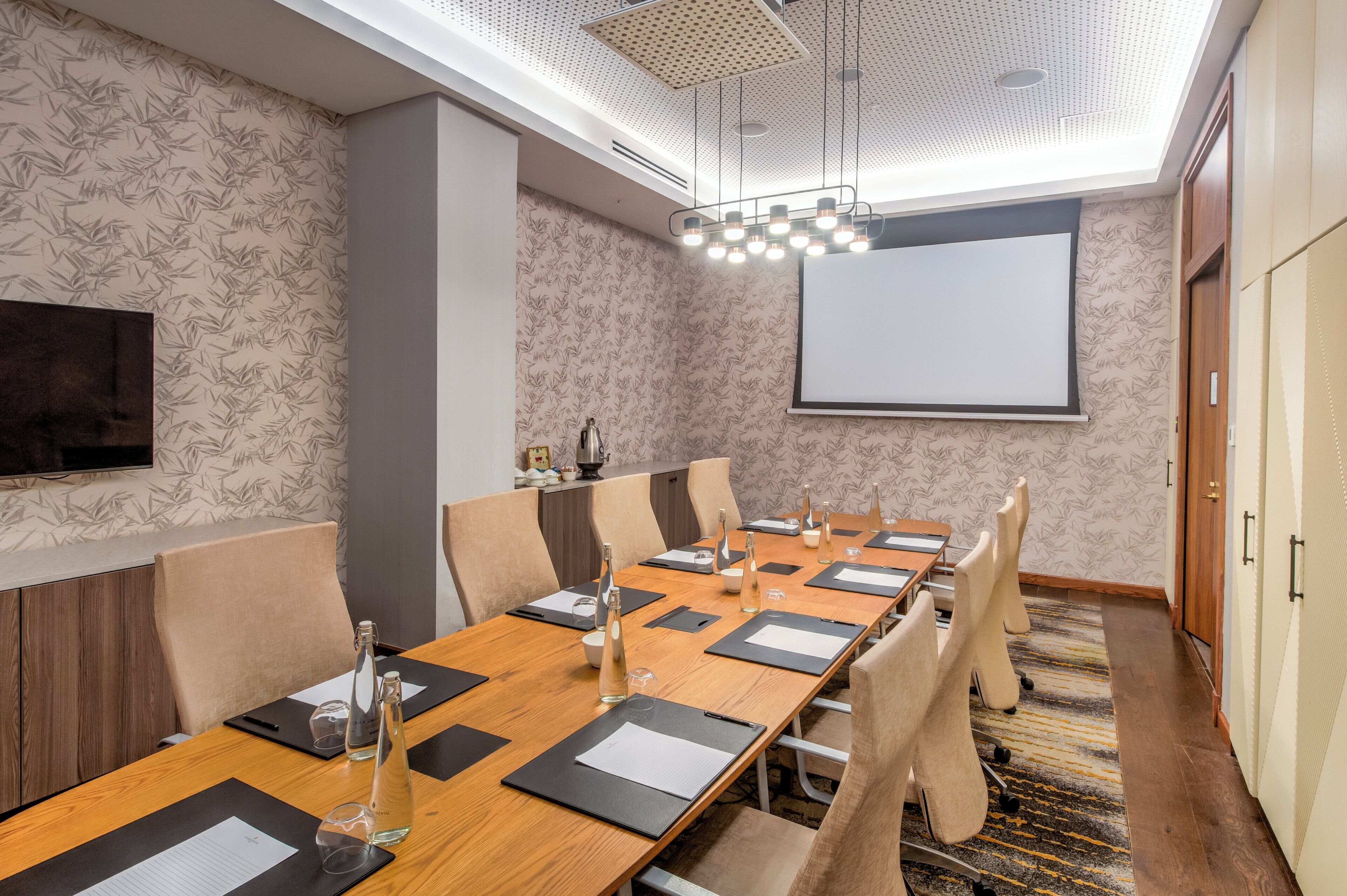 A conference room with a long table, chairs, a projector screen, and a television.