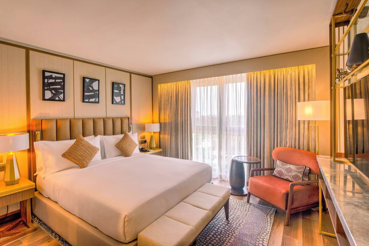 A spacious hotel room with a large bed, a sitting area with a chair, and a desk.