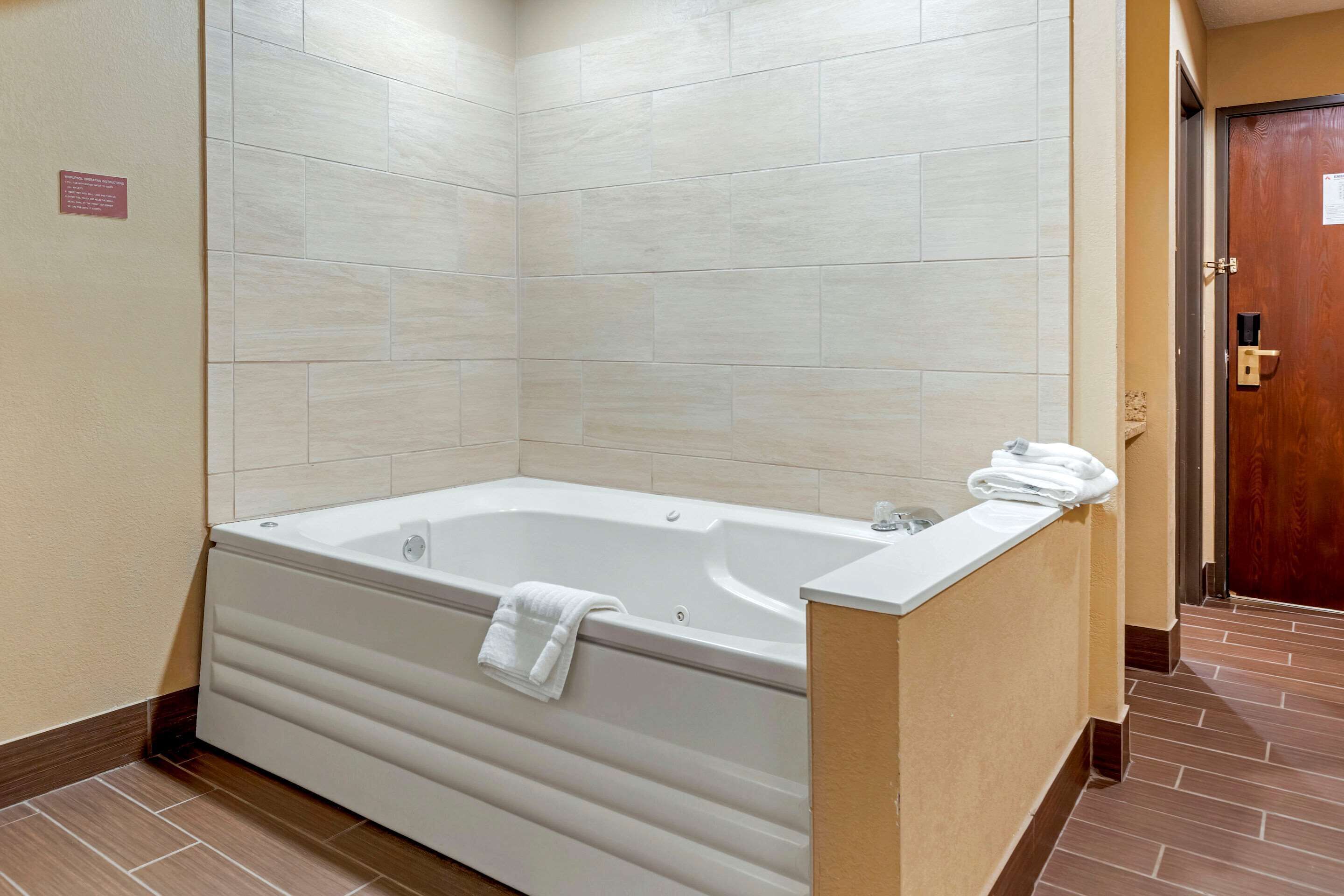 A modern bathroom with a large bathtub, a wooden door, and a tiled floor.