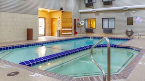 An indoor swimming pool with a tiled edge, a lifeguard on duty sign, and a wooden bench area.