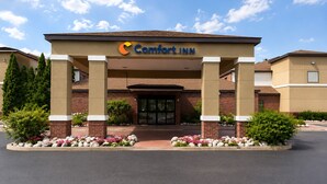 A Comfort Inn hotel entrance with a brick facade, a covered entrance area, and landscaped flower beds.