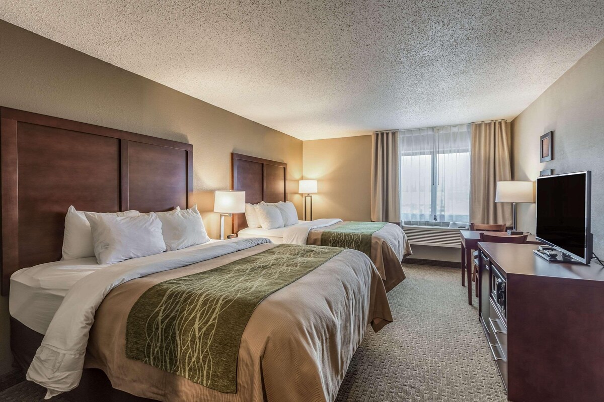 A hotel room with two beds, a desk, a TV, and a window with curtains.
