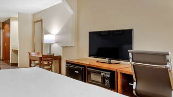A hotel room with a bed, a desk with a television, a lamp, and a microwave.