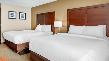 A hotel room with two single beds, a wooden headboard, a nightstand with a lamp, and two framed pictures on the wall.