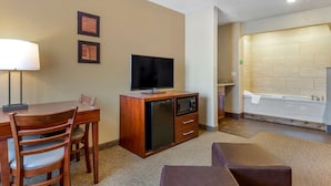 A hotel room with a dining area, a TV, a minibar, and a bathtub.
