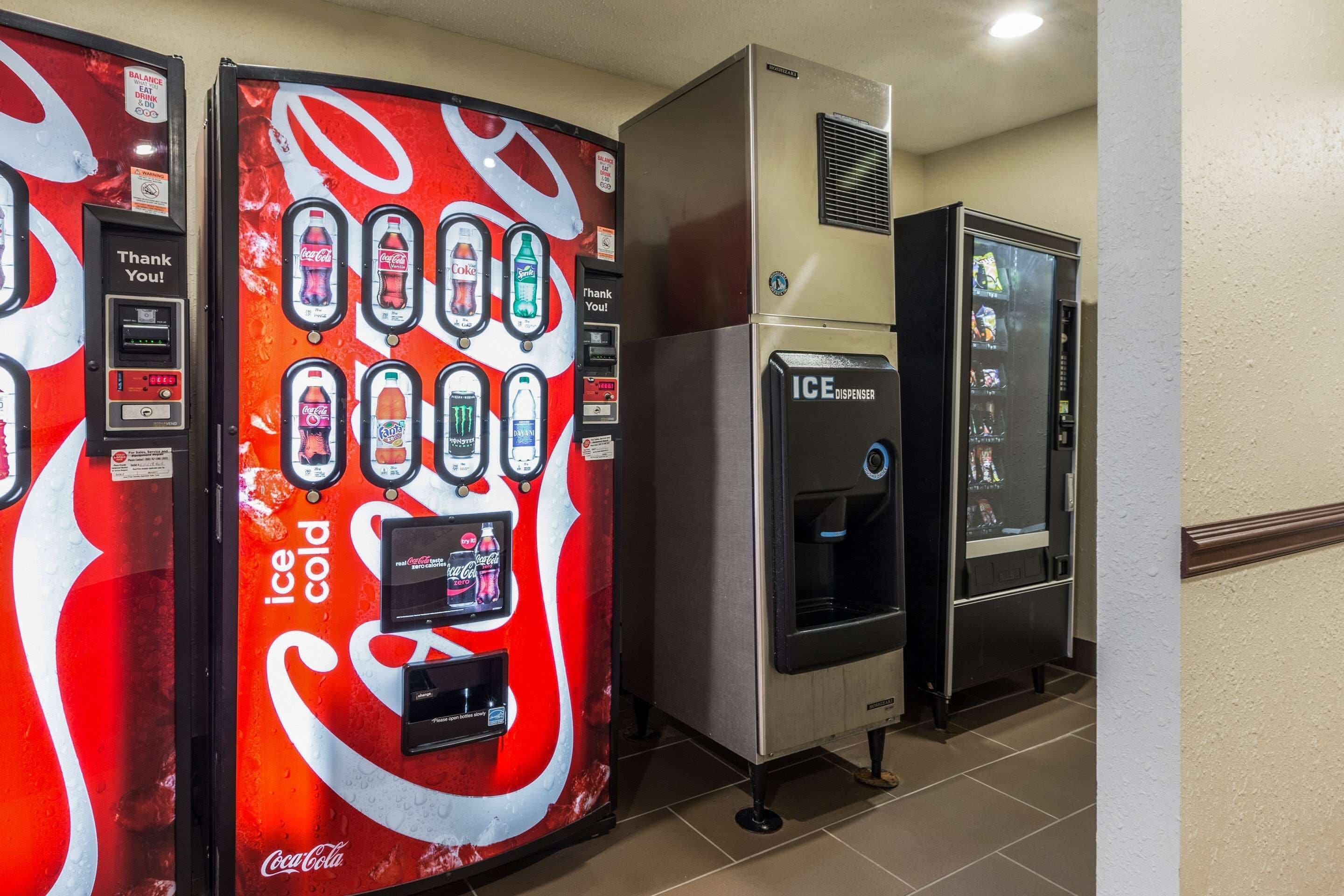 Uma fileira de máquinas de venda automática, incluindo uma máquina de gelo com a marca Coca-Cola e um dispensador de gelo.
