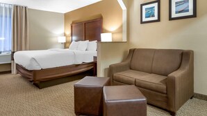 A hotel room with a bed, a sofa, and a small ottoman. There are two framed pictures on the wall.