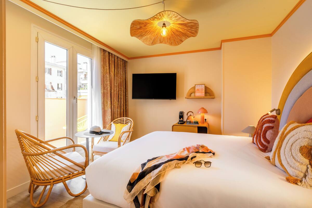 A hotel room with a bed, a television, a small table with a chair, and a window with curtains.
