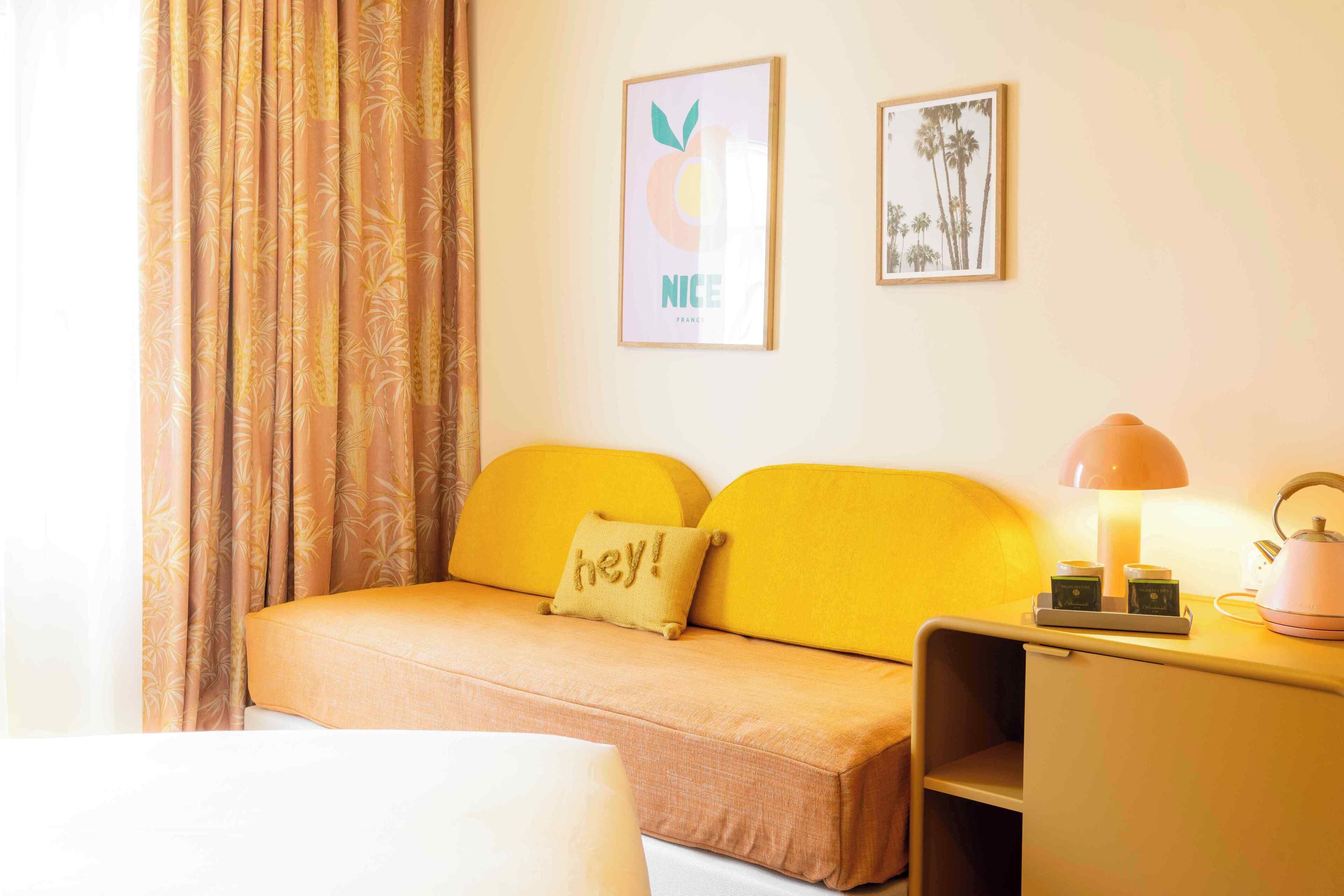 A room with a sofa, a bed, a desk with a lamp, and two framed pictures on the wall.