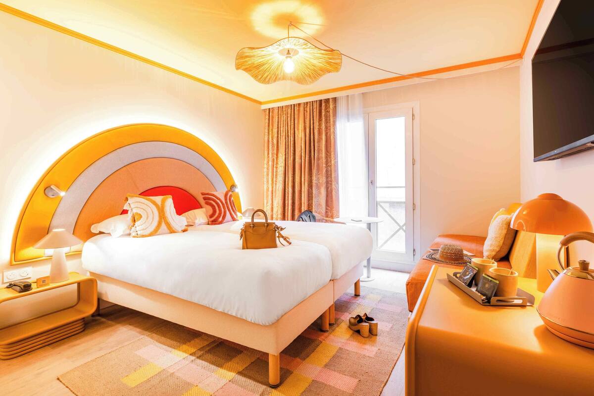A hotel room with a bed, bedside table, lamp, and a view of the outdoors.
