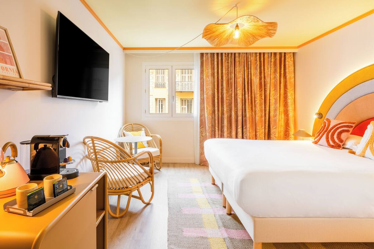 A hotel room with a bed, a desk with a coffee maker, a television, and a window with curtains.