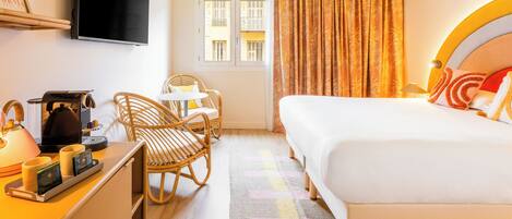 A hotel room with a bed, a desk with a coffee maker, a television, and a window with curtains.