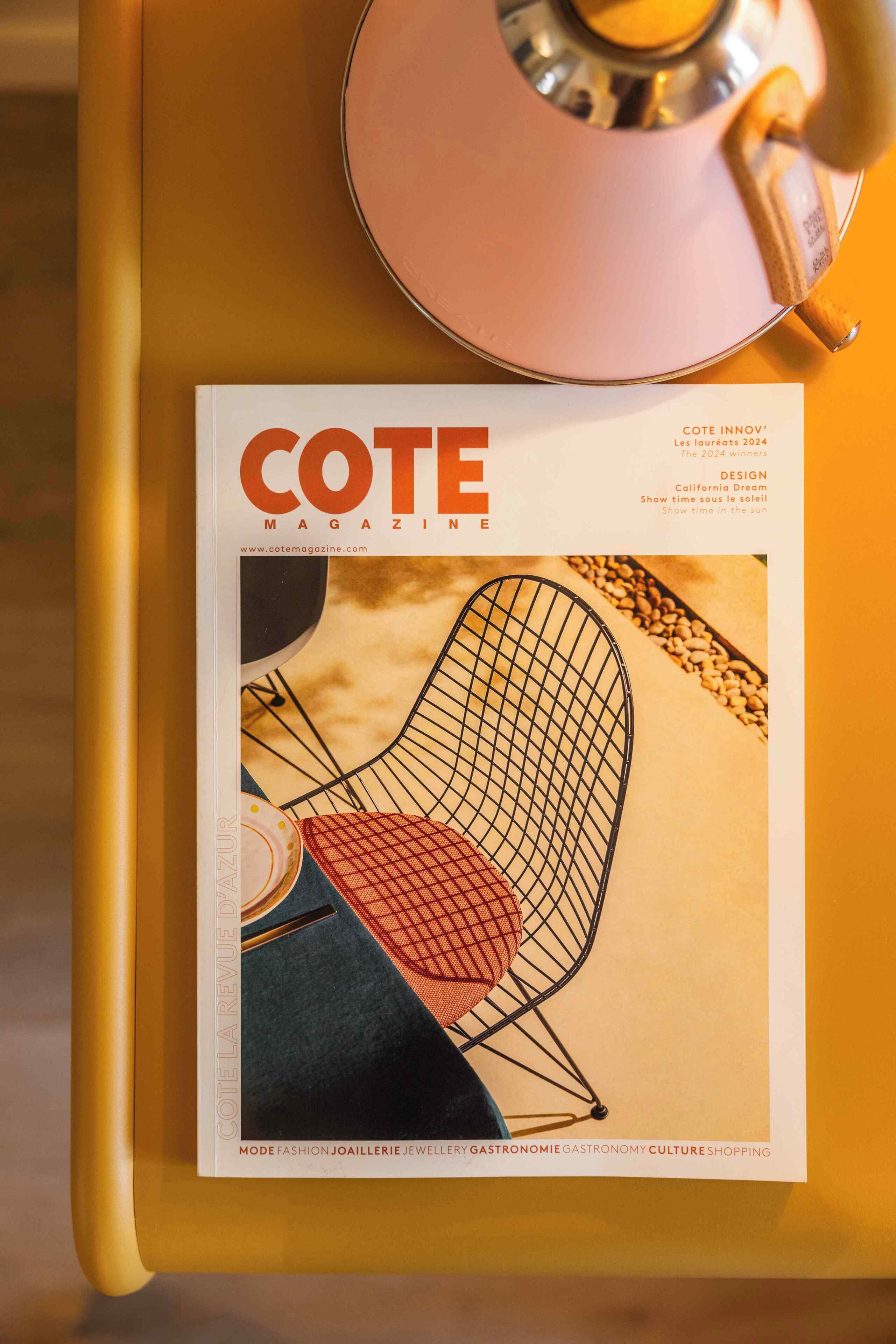 Portada de revista con énfasis en una silla de estructura metálica y un cojín rojo, sobre una superficie amarilla.