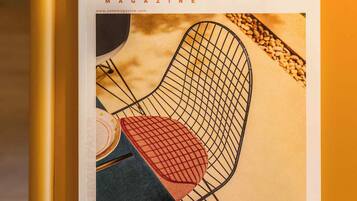 Portada de revista con énfasis en una silla de estructura metálica y un cojín rojo, sobre una superficie amarilla.