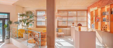 A modern reception area with a wooden reception desk, a seating area with a yellow chair and a small table, and a wall with a 'Welcome' sign and a calendar.