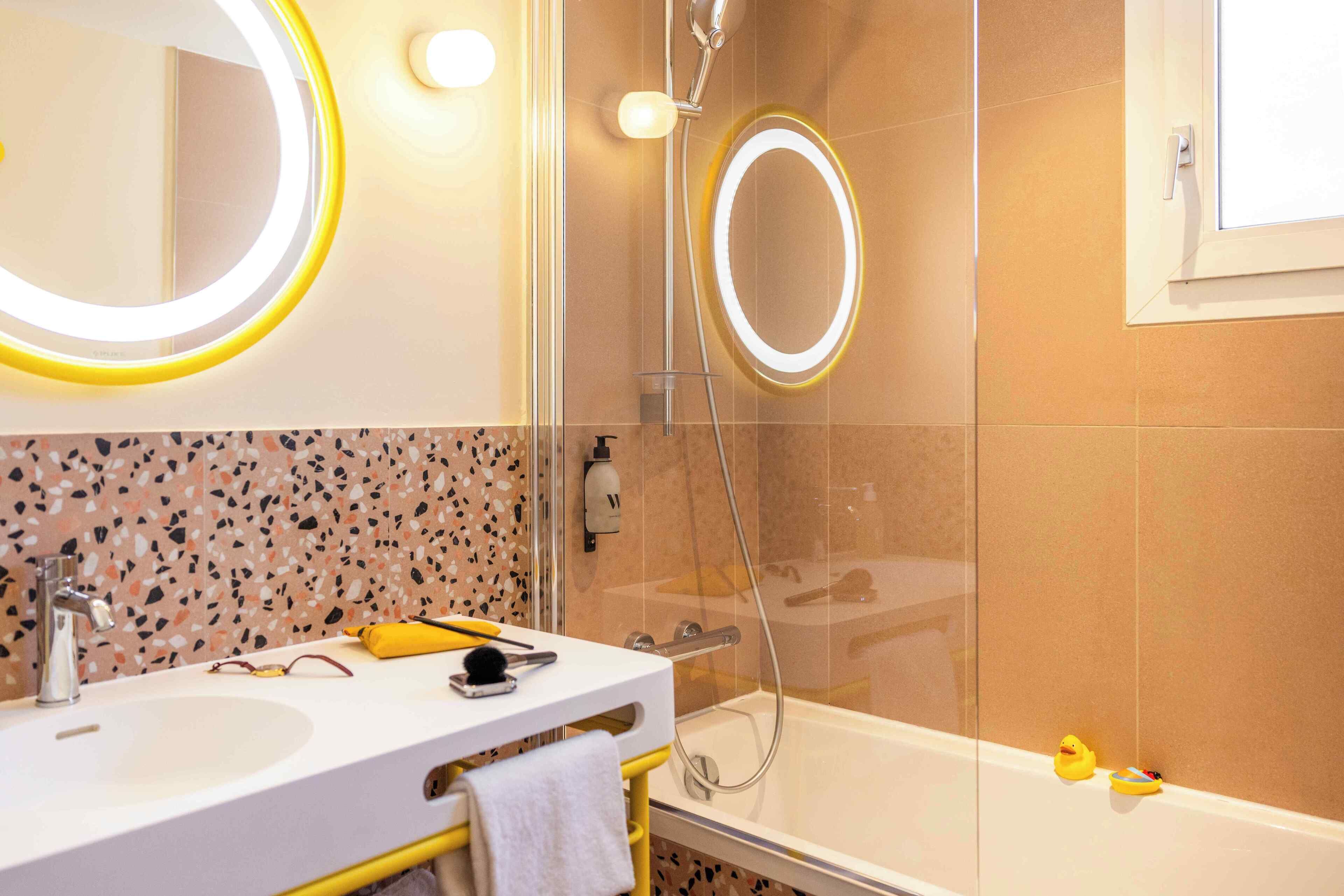 A modern bathroom with a glass-enclosed shower, a white sink, and a mirror with a ring light.