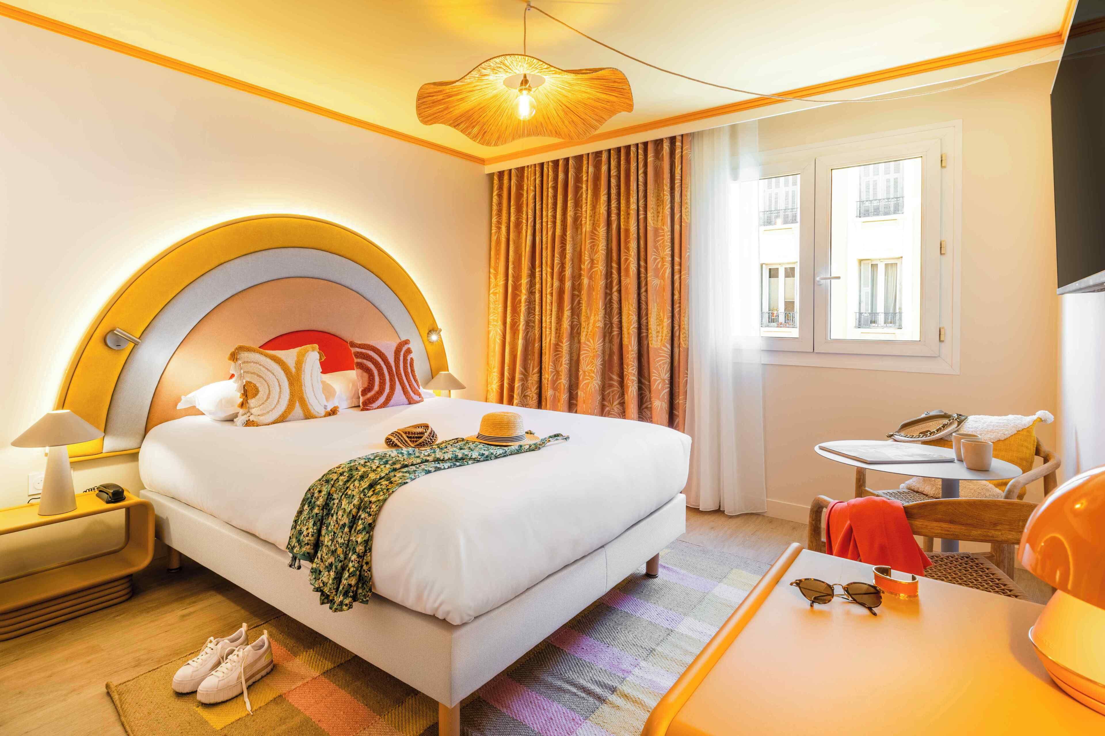 A hotel room with a large bed, a small table, a chair, a nightstand, and a window with curtains.