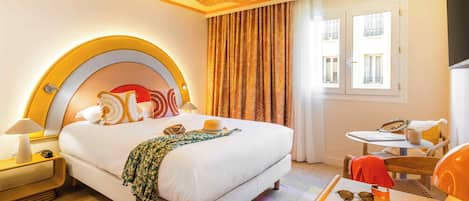A hotel room with a large bed, a small table, a chair, a nightstand, and a window with curtains.