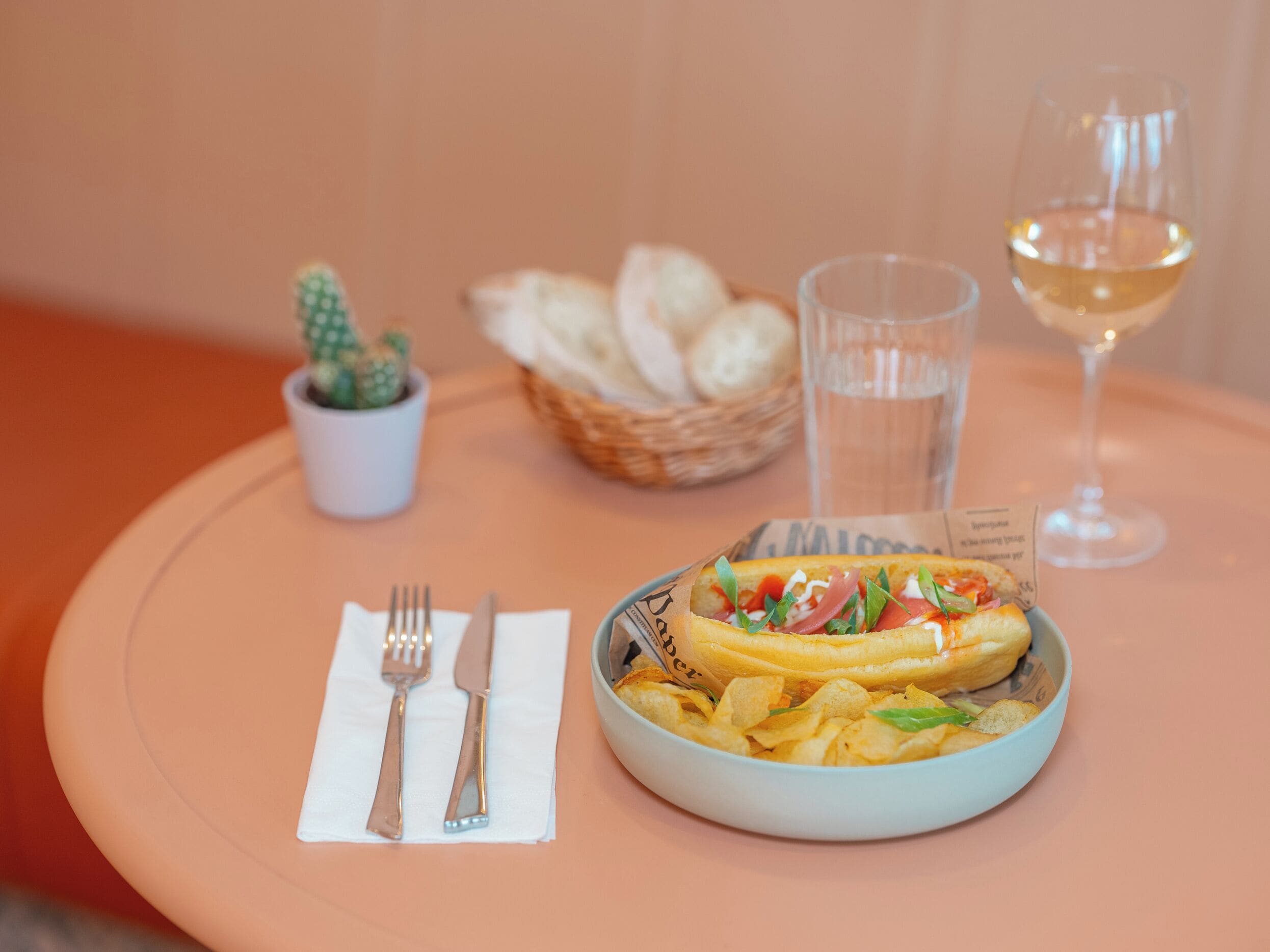 Un plato de comida con patatas fritas, una copa de vino blanco y una cesta de pan sobre una mesa.