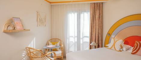 A hotel room with a bed, a chair, a small table, a macrame wall hanging, and a macrame shelf.