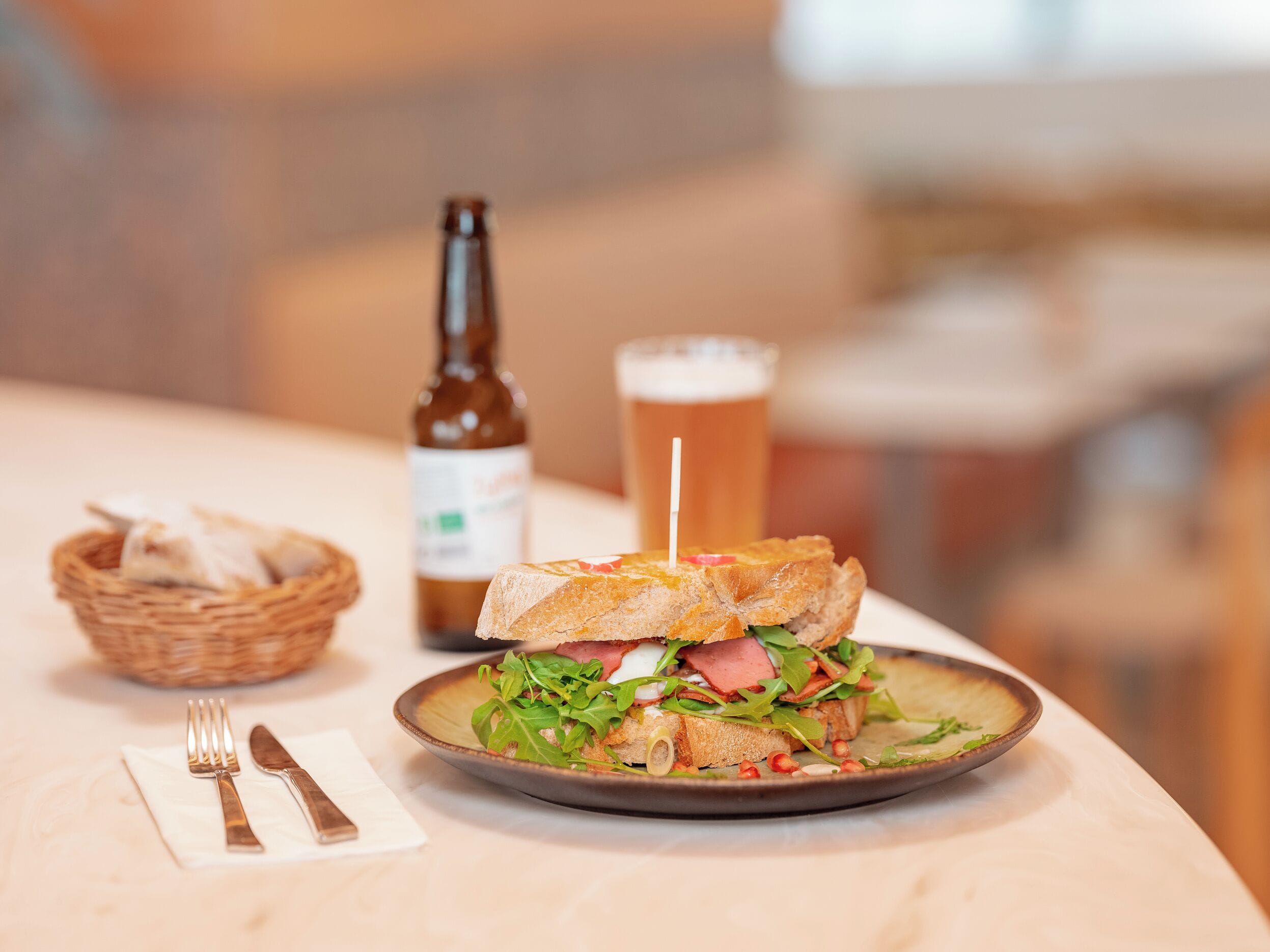Un panino su un piatto, con una bottiglia e un bicchiere di birra sullo sfondo.