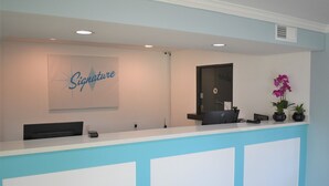 A reception desk with a 'Signature' sign, a computer, a phone, and a potted plant. - Signature Anaheim Maingate (Anaheim)