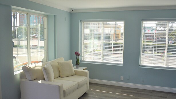 A room with a white sofa, large windows, and a view of the outside. - Signature Anaheim Maingate (Anaheim)