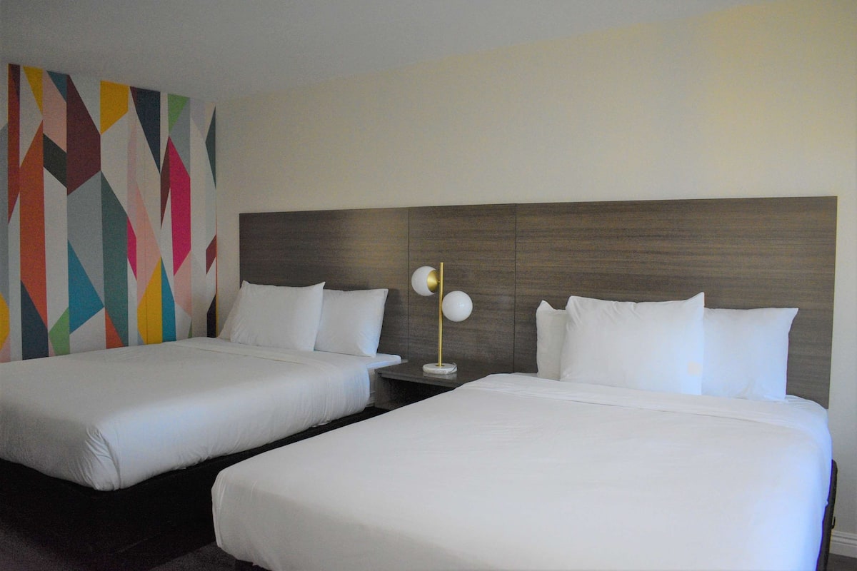 Habitación de hotel con dos camas, un cabecero moderno y un diseño de pared geométrico y colorido.