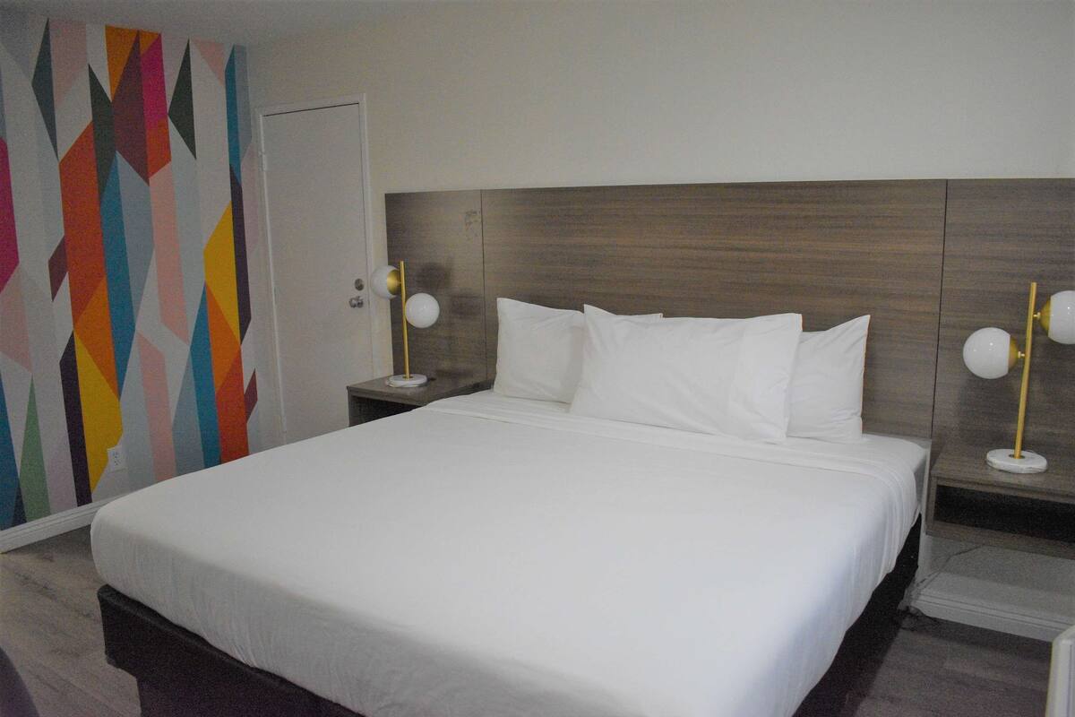 Una cama bien hecha con ropa de cama blanca, un cabecero de madera y dos mesitas de noche con lámparas.