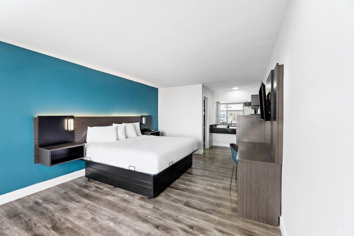 A modern hotel room with a large bed, a built-in TV, and a wooden floor.