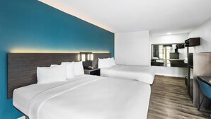 A hotel room with two beds, a desk, a mirror, and a bathroom visible in the background.