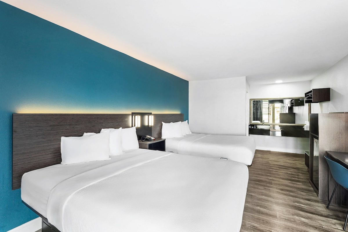 A hotel room with two beds, a desk, a mirror, and a bathroom visible in the background.