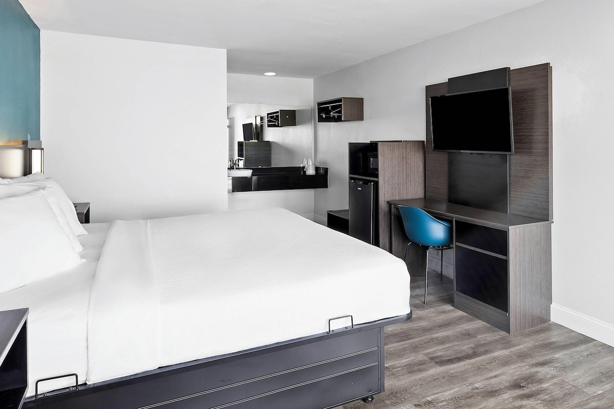 Una habitación de hotel moderna con cama, escritorio, televisor y espejo.