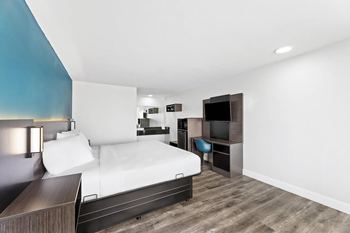 A modern hotel room with a bed, desk, chair, and built-in TV.