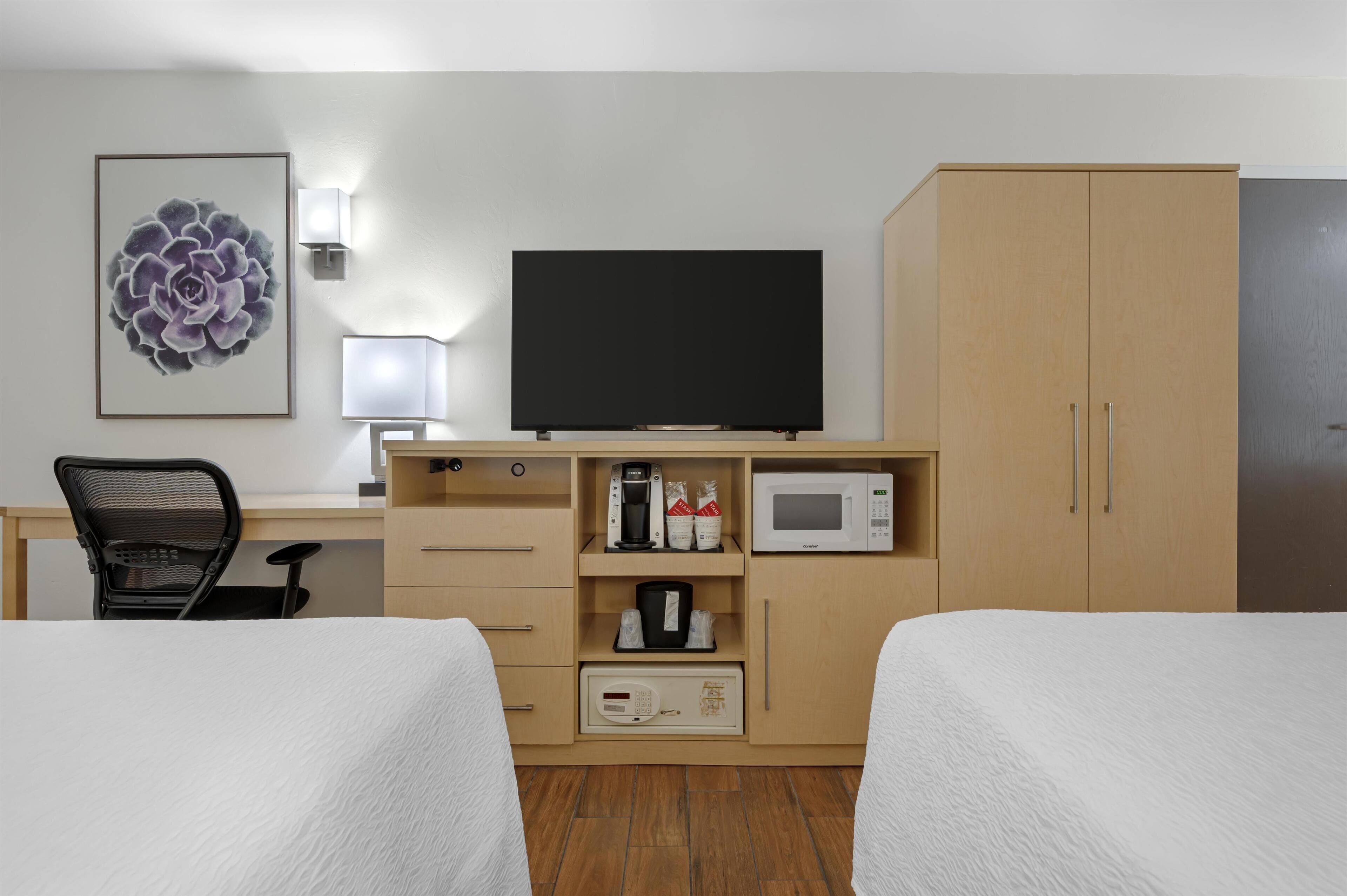 Habitación de hotel con dos camas, un escritorio con computadora, televisión, microondas y cafetera.