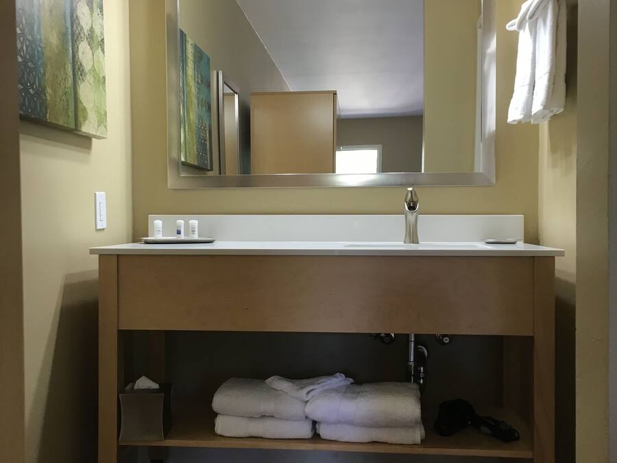 A bathroom with a large mirror, a sink, and a shelf under the sink.