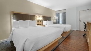 Ein Hotelzimmer mit zwei Betten, einem Holzkopfteil, Nachttischlampen, einem Schreibtisch und einem Sessel.