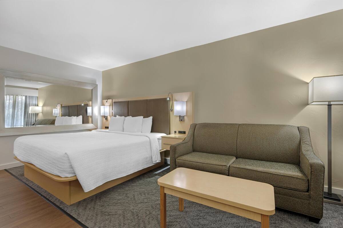A hotel room with a large bed, a sofa, a table, and a lamp.