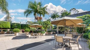 Ein Außenbereich mit Terrasse, belegter Fläche, mehreren Tischen und Stühlen sowie Sonnenschirmen als Sonnenschutz.
