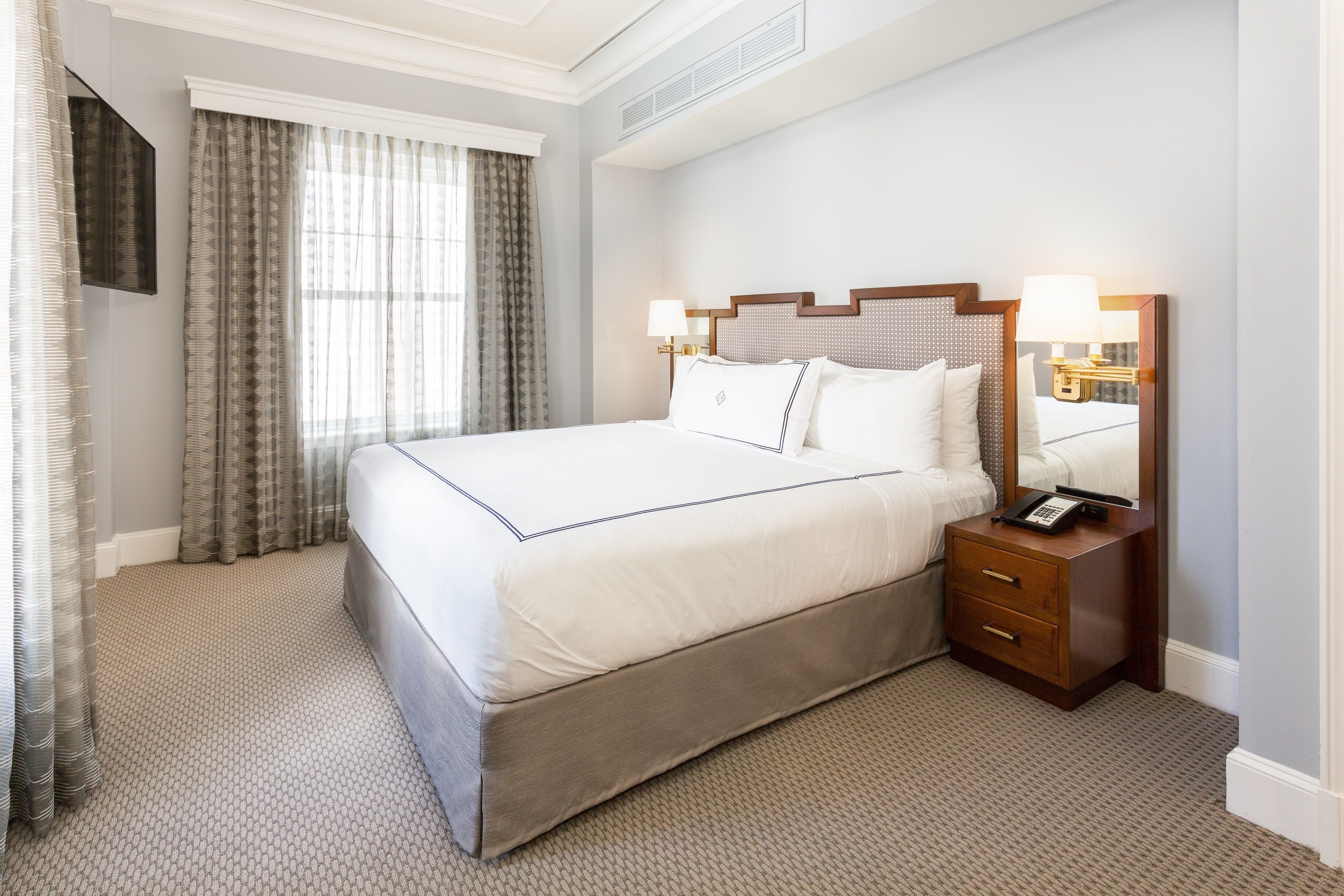 A neatly made bed with a wooden headboard, a bedside table with a lamp, and a mirror.