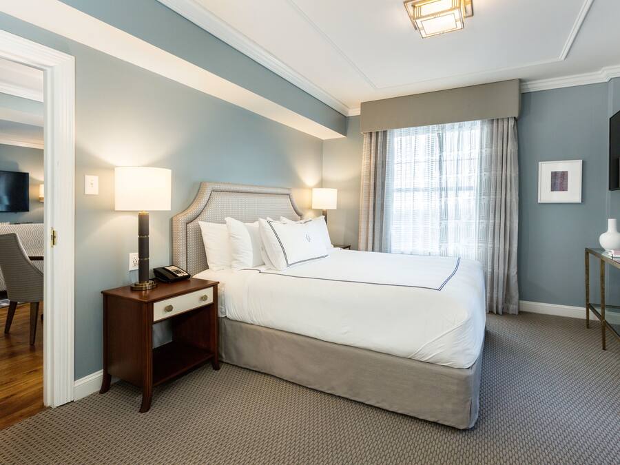 Quarto de hotel com cama grande, luminárias de cabeceira, televisão de tela plana e uma mesinha com um vaso.