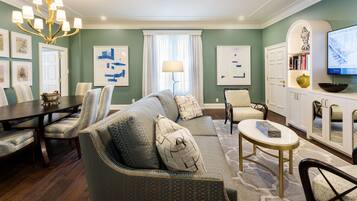 A living room with a dining table, sofa, chairs, a chandelier, and a television.