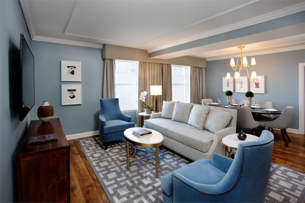 A modern living room with a sofa, two armchairs, a coffee table, and a dining area with a chandelier.