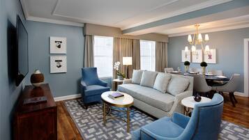 A modern living room with a sofa, two armchairs, a coffee table, and a dining area with a chandelier.